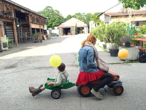 Girl on model tractor pulls trailer with little boy Stockfoto's