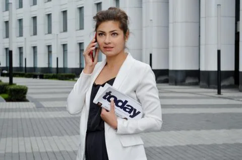 A girl with a newspaper in her hands is talking on the phone on the city stre Stock Photos