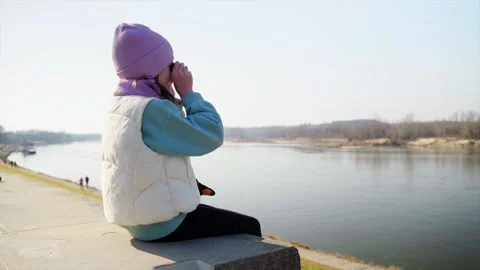 A girl observes a river with binoculars, sharing the moment with a woman Stock Footage 304863539