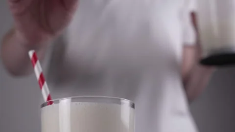 A girl, out of focus, throws fresh strawberries into a glass with a milkshake. Stock Footage 276267997
