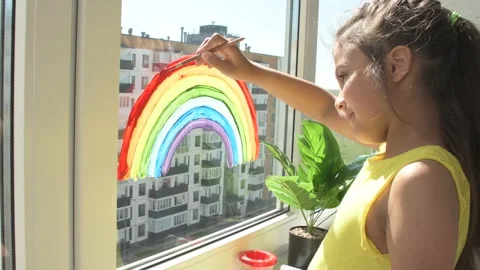 Girl painting rainbow on window during quarantine at home. Stock Footage