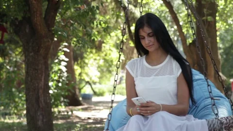 Girl in park on swing, with smartphone Stock Footage