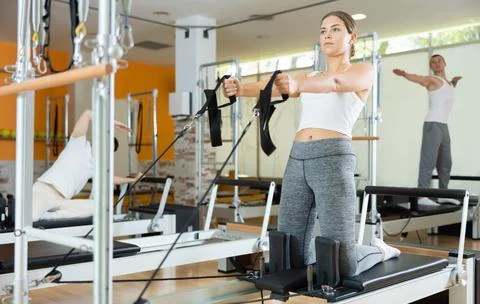 Girl performing pulling straps exercise on Pilates reformer Stock Photos