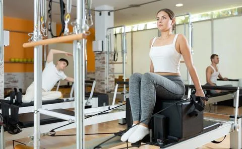 Girl performing pulling straps exercise on Pilates reformer with box Stock Photos
