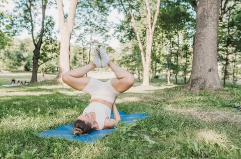 The girl performs complex yoga exercises in the park on a gym mat. the concep Stock Photos