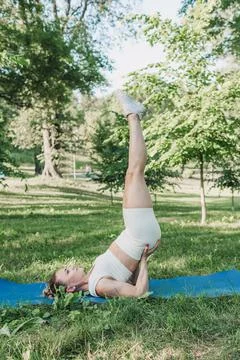 The girl performs complex yoga exercises in the park on a gym mat. the concep Stock Photos