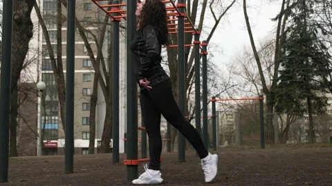 A girl performs an exercise on swinging her legs on a sports field on the street Stock Footage 237992487