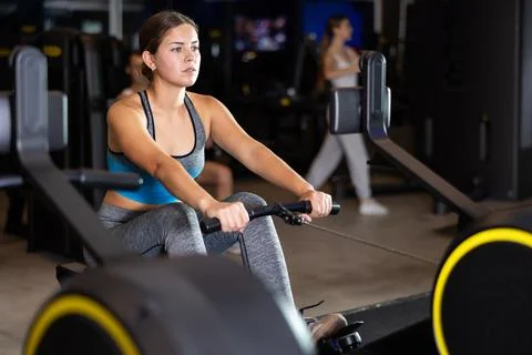Girl performs exercises with rowing machine in gym Photos