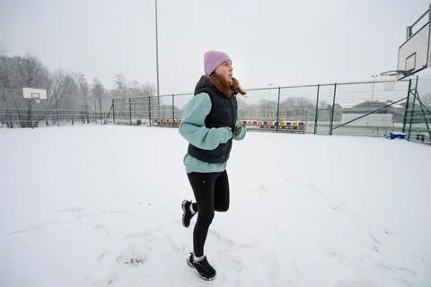 Girl performs a running in place exercise on a snowy sports ground in winter. Stock Photos