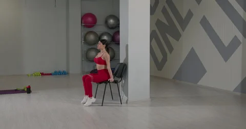 Girl performs seated leg raises with resistance band in a bright gym environment Vídeos de archivo 310174876