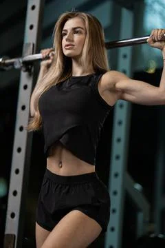 Girl performs squat exercise with barbell in modern gym setting during daylight Stock Photos
