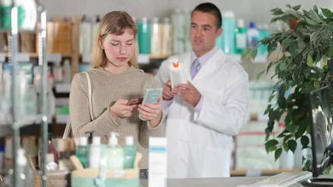 Girl in pharmacy scans QR code on emollient for sensitive skin, male pharmacist Stock Footage 322118096