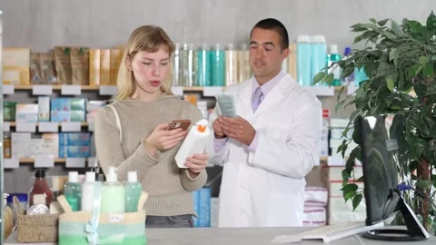 Girl in pharmacy scans QR code on emollient for sensitive skin, male pharmacist Stock Footage 344774046