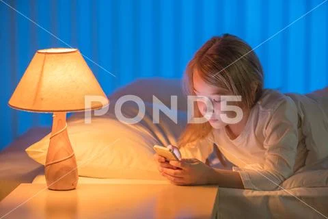 The girl with a phone lay on the bed. Evening night time Stock Photos