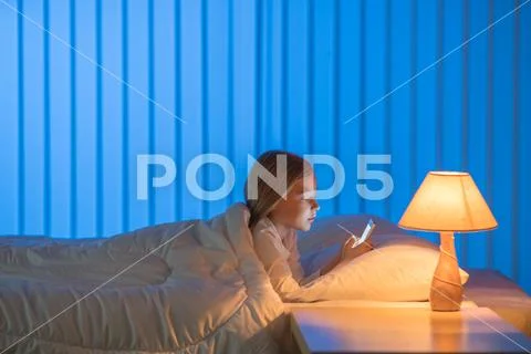 The girl with a phone lay on the bed. Evening night time Stock Photos