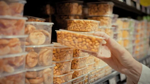 A girl picks up a packaged container of mixed nuts from a store shelf surrou Stock Footage 341491012