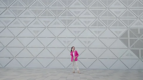 A girl in a pink jacket and light trousers is talking on the phone in front of Stock Footage 242567053