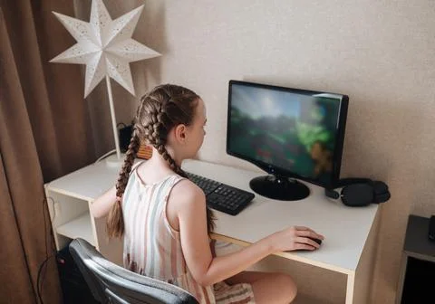 Girl playing on computer, holding mouse and looking at monitor with focus Stock Photos