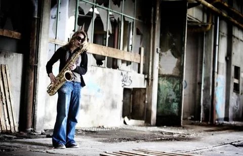 Girl playing saxophone in old factory hall. Stock Photos