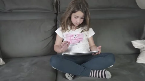 Girl playing with tablet sitting on sofa at home Stock Footage 239192243