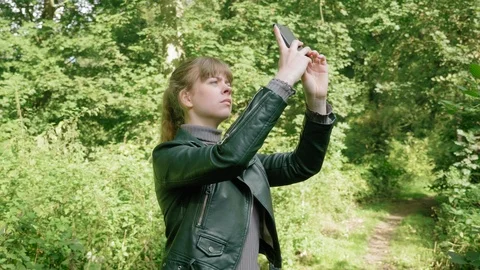 Girl points phone up with camera app for photo in woods, tracking Stock Footage 123770147