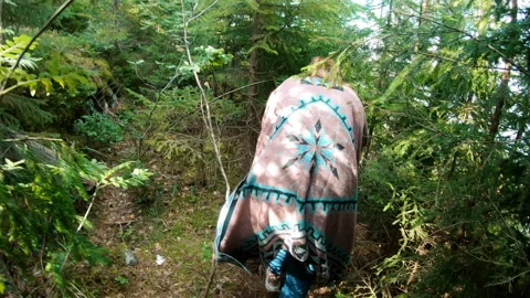A girl in a poncho with difficulty makes her way through the thickets in forest Stock Footage 200780743