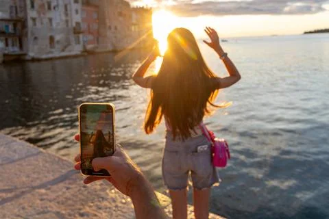 Girl posing at sunset while being photographed by phone. A teenage girl poses Stock Photos