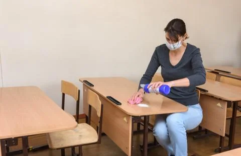 The girl pours cleaning and disinfectant on the desk at the school during the Stock Photos