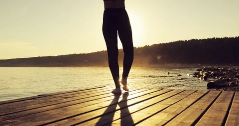 Girl is practicing yoga in Tree Pose standing on the pier at yellow sunset. Stock Footage 112043304