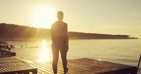 Girl practicing yoga in Tree Pose standing on the pier at sunset, back view. Stock Footage 112043441