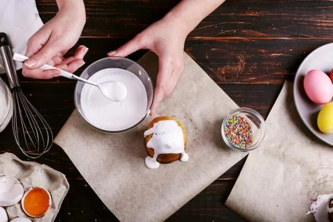 The girl prepares Easter baking, smears the cake with icing and sprinkles wit Stock Photos