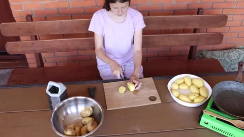 Girl preparing potatoes for cooking in a rustic kitchen setting Stock Footage 297358742