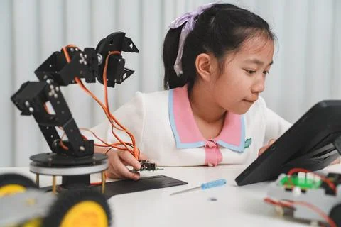 A girl programs a robot with a tablet. Engineering, technology, and learning. Stock Photos