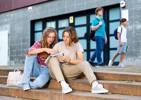 Girl prompts solution to problem to young man sitting on stone staircase in Stock Photos