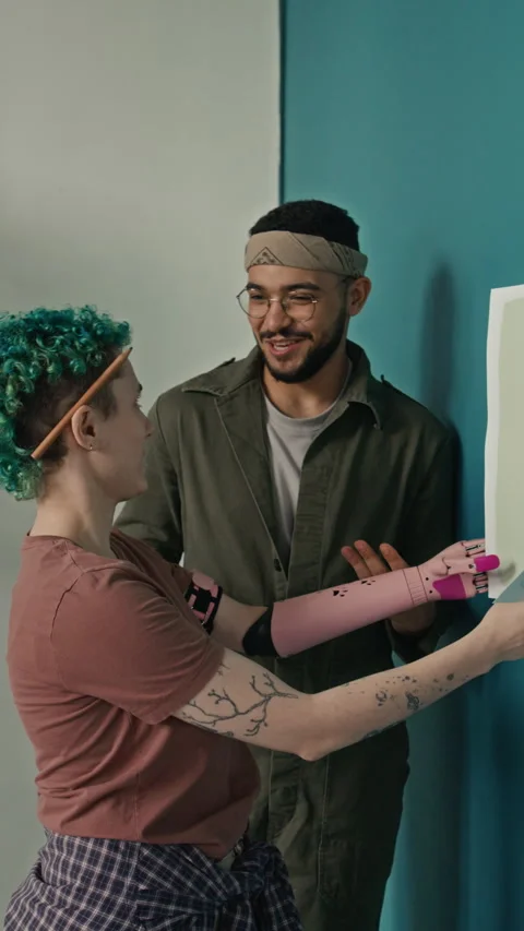 Girl with Prosthesis Holding Two Papers Choosing Paint Color with Boyfriend Stock Footage 323311144