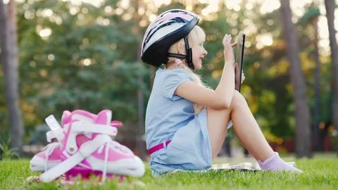 A girl in a protective helmet is playing on a tablet, next to her are roller Stock Footage 80052288