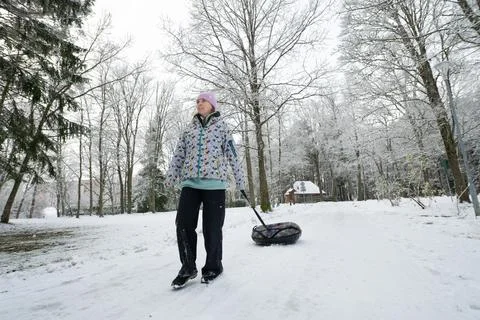Girl pulling inflatable donut sled through a scenic snowy winter park. Stock Photos