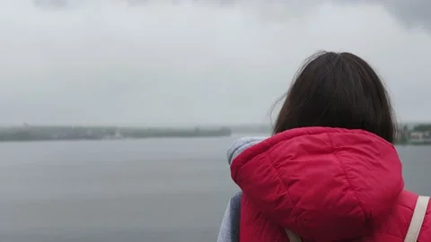 Girl pulls red hood over her head in drizzling rain next to river. Stock Footage 134698003