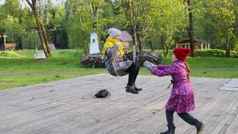 Girl pushes playmate which sways on swing at summer day in country club. Slow Stock Footage 276368024