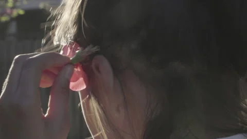 Girl puts pink flower behind her ear as an ornament, pulls up her hair and walks Stock Footage 142769953