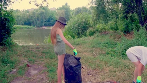 Girl putting plastic bottle into garbage bag near tree Stockbeeldmateriaal 340464780