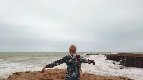 Girl raises her hands up while standing with her back on the seashore during a Stock Footage 133790613