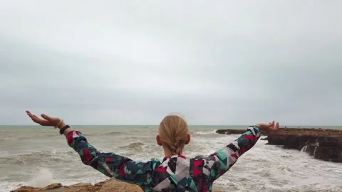 Girl raises her hands up while standing with her back on the seashore during a Stock Footage 133794775