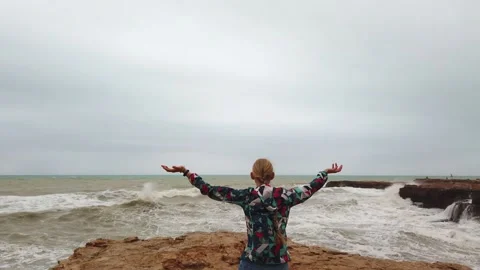 Girl raises her hands up while standing with her back on the seashore during a Stock Footage 133801183
