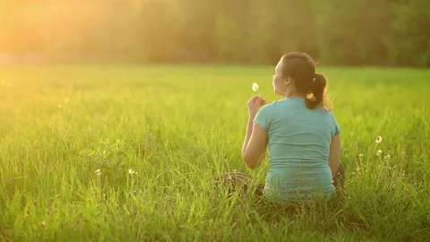 Girl in the rays of the setting sun blows on a dandelion Stock Footage 203763028