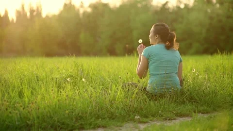 Girl in the rays of the setting sun blows on a dandelion 스톡 동영상 203763104