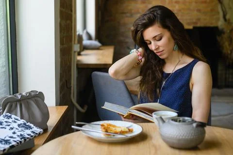 Girl reading a book while having breakfast in a coffee shop Stock Photos