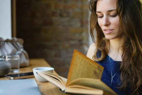 Girl reading a book while having breakfast in a coffee shop Stock Photos