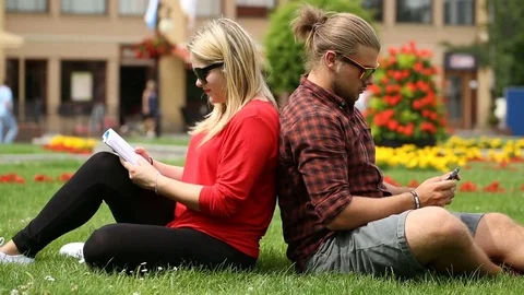 Girl reading book while her boyfriend is playing game on smartphone Stock Footage 77476345
