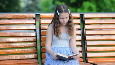 Girl reading a book while sitting on the bench Stock Footage 77664865